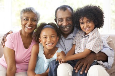 Grandparents With Grandchildren Relaxing On Sofa At Home Togethe clipart