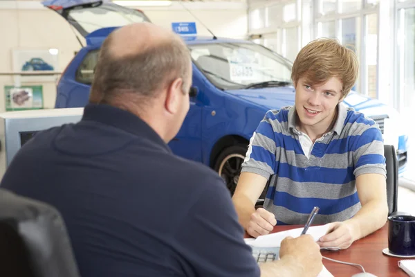 Young man filling in paperwork in car showroom — Stockfoto
