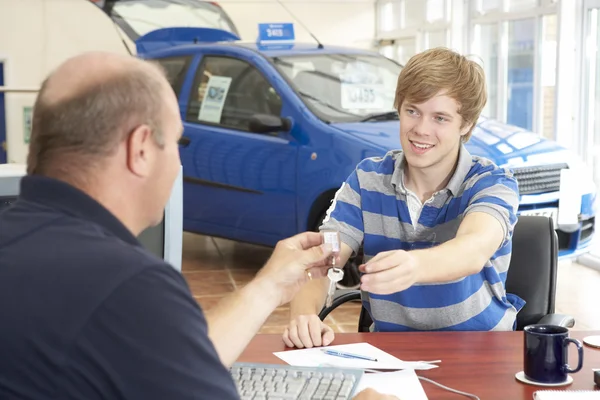 Young man filling in paperwork in car showroom — Stock Photo, Image