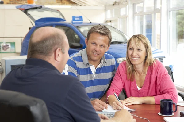 Couple filling in paperwork in car showroom — Stock Photo, Image