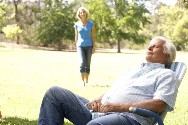 Hombre mayor que se relaja en el parque con su esposa en segundo plano —  Fotos de Stock