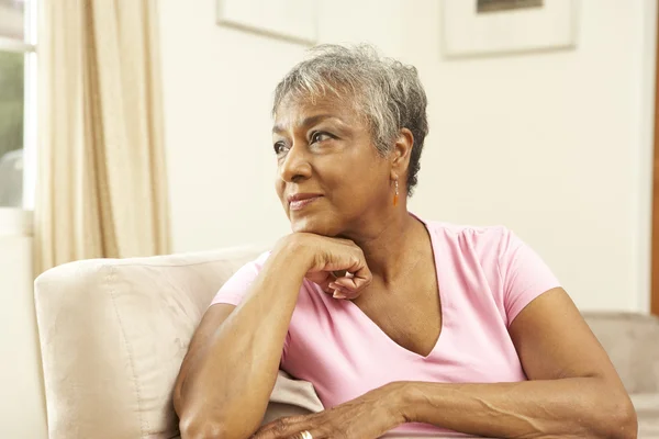 Senior mulher olhando pensativo na cadeira em casa — Fotografia de Stock