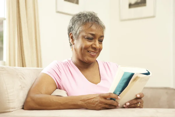 Starší žena čte doma knihu — Stock fotografie