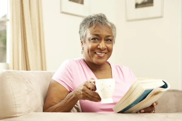 Старшая Женщина Читает Книгу Напитком Дома — стоковое фото