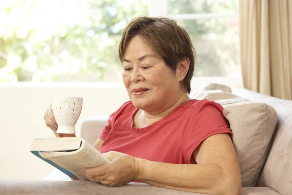年配の女性が自宅でドリンクを飲みながら本を読んで — ストック写真