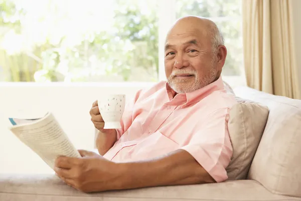 Starszy Człowiek Czytając Książkę Przy Drinku Domu — Zdjęcie stockowe