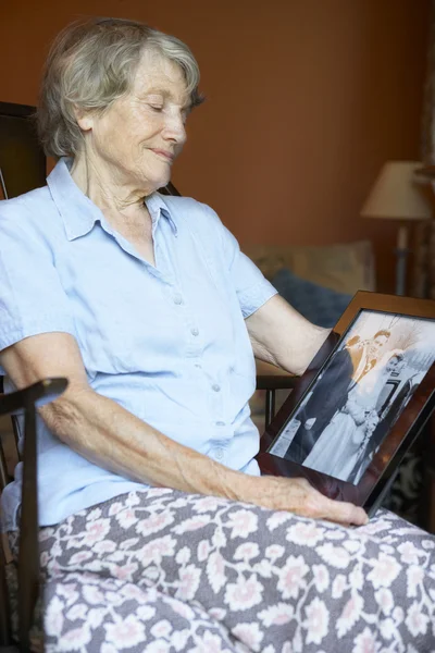 Senior vrouw thuis kijken naar oude bruiloft foto — Stockfoto