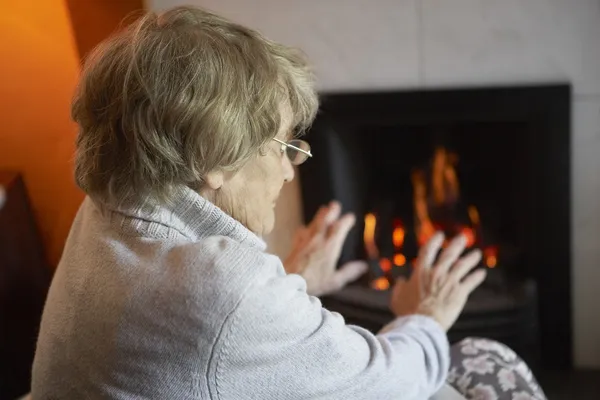 Anziana donna riscaldamento mani da fuoco a casa — Foto Stock