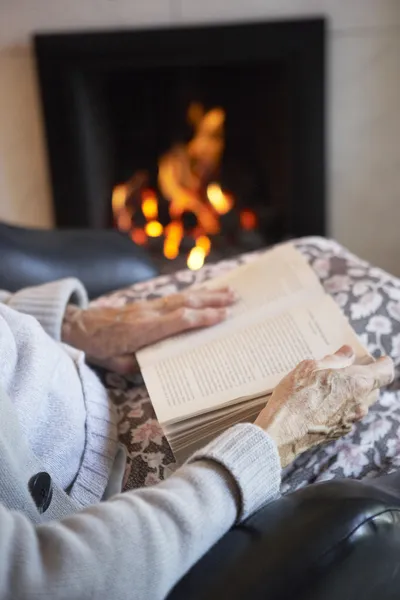 Detalii despre o femeie în vârstă care citește cartea cu foc acasă — Fotografie, imagine de stoc