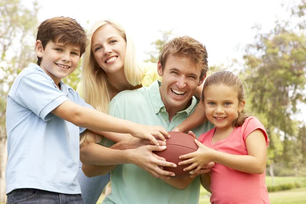 Family Playing American Football Together In Park Stock Photo