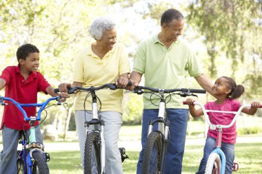 Grandparents In Park With Grandchildren Riding Bikes clipart