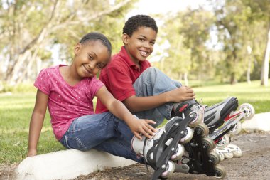 Children Putting On In Line Skates In Park clipart