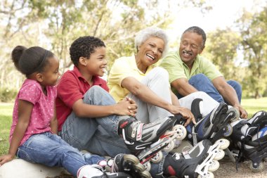 Grandparent With Grandchildren Putting On In Line Skates In Park clipart