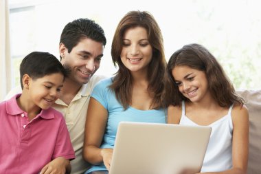 Family Sitting On Sofa At Home With Laptop clipart