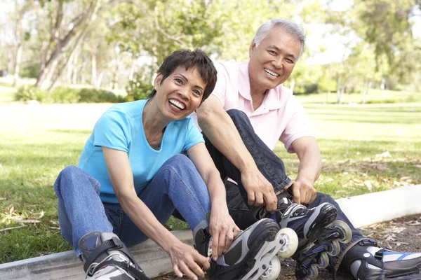 Seniorenpaar schnallt im Park Inlineskates an — Stockfoto