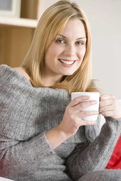 Ung kvinna sitter på soffan med kopp kaffe — Stockfoto