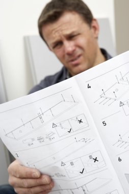 Puzzled Man Reading Assembly Instructions For Flat Pack Furnitur clipart