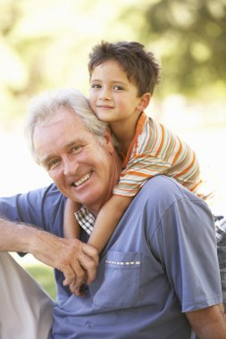Grandfather Giving Grandson Ride On Back In Park clipart