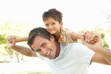 Father Giving Son Ride On Back In Park clipart