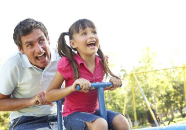 Father And Daughter Riding On See Saw In Playground clipart