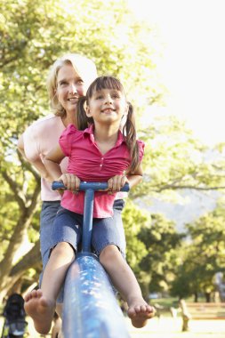 Grandmother And Granddaughter Riding On See Saw In Playground clipart