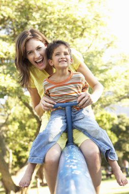 Mother And Son Riding On See Saw In Playground clipart