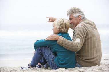 Grandfather And Son Sitting On Winter Beach Together clipart