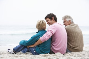 Grandfather, Father And Grandson Sitting On Winter Beach clipart