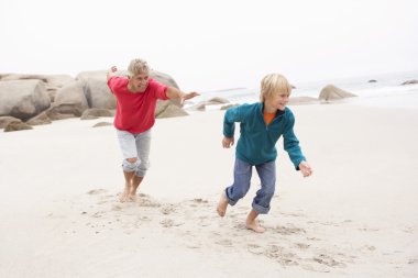 Grandfather Chasing Grandson Along Winter Beach clipart