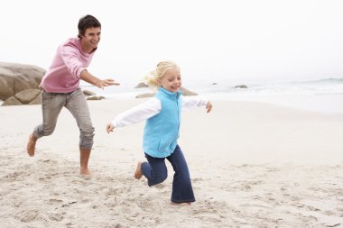 Father Chasing Daughter Along Winter Beach clipart