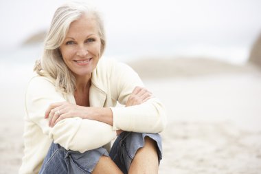 Senior Woman On Holiday Sitting On Winter Beach clipart