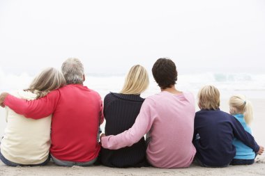 Back View Of Three Generation Family Sitting On Winter Beach Tog clipart