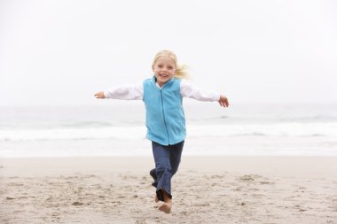 Young Girl On Holiday Running Along Winter Beach clipart