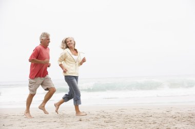 Senior Couple On Holiday Running Along Winter Beach clipart