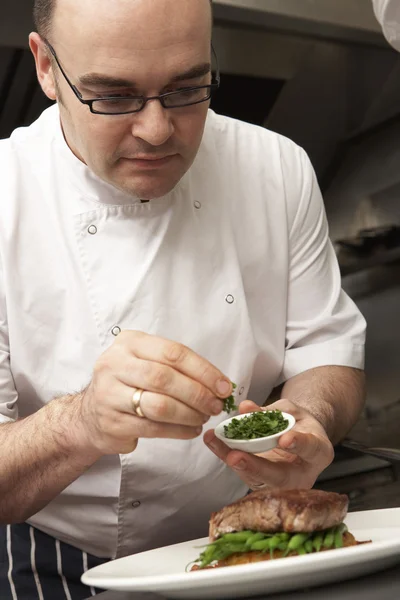 Šéfkuchař přidání koření jídlo v kuchyni restaurace — Stock fotografie