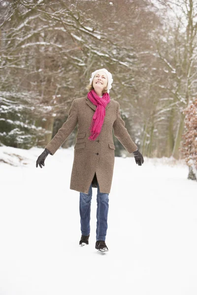 Äldre kvinna gå genom snöiga skogsmark — Stockfoto