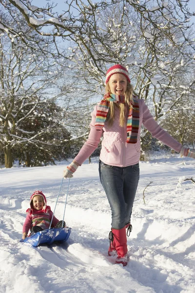 Mamma drar dotter på släde genom snöiga landskap — Stockfoto