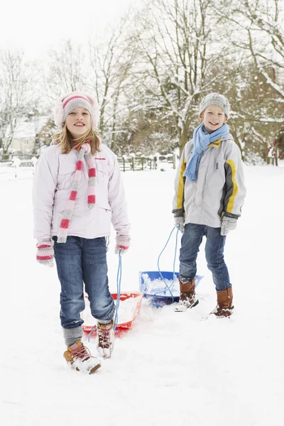 Crianças puxando o trenó através da paisagem nevada — Fotografia de Stock
