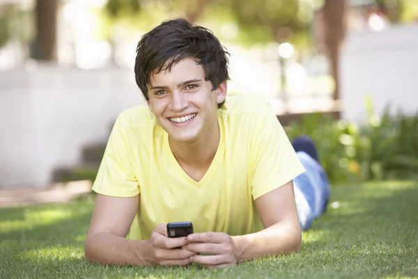 Adolescente yaciendo en el parque usando teléfono móvil — Foto de Stock