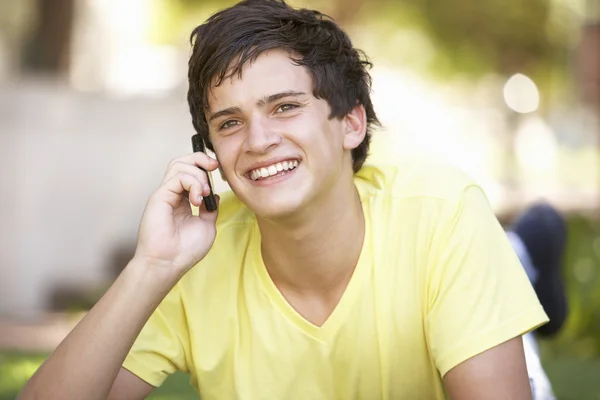 Tizenéves fiú fektetése park mobiltelefon használata — Stock Fotó