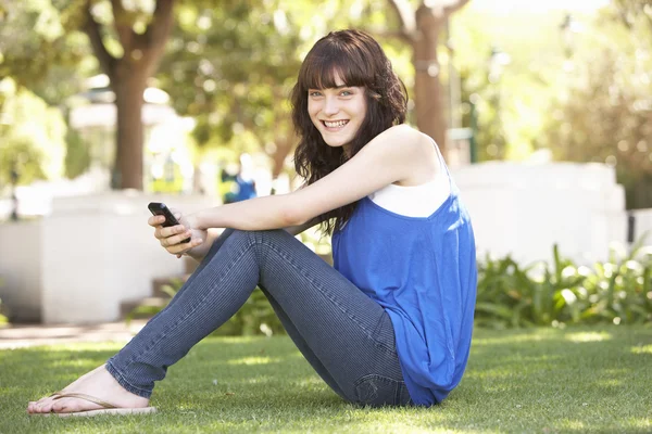 携帯電話を使用して公園で座っている 代の少女の肖像画 — ストック写真