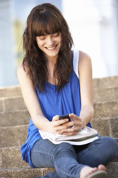Подросток, сидящий снаружи на ступеньках колледжа, используя мобильный телефон — стоковое фото
