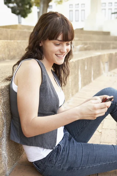 Подросток, сидящий снаружи на ступеньках колледжа, используя мобильный телефон — стоковое фото