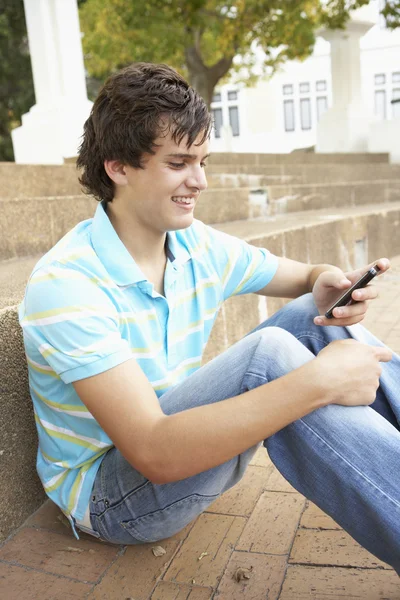 Hombre adolescente estudiante sentado fuera en la universidad pasos usando Mobi —  Fotos de Stock