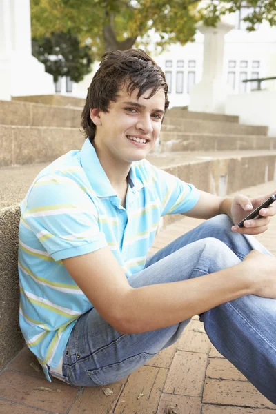 坐在外面上大学步骤使用手机的男性青少年学生 — 图库照片