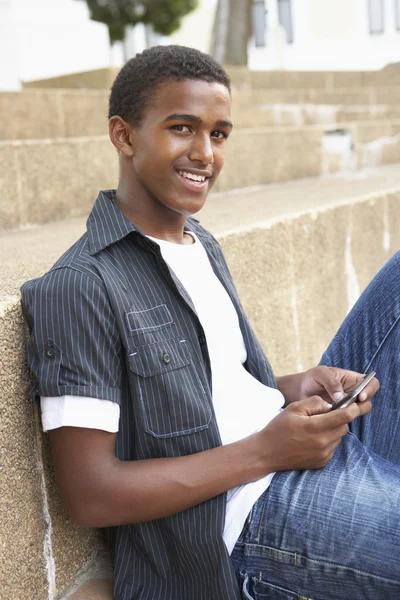 Männlich teenager student sitting draußen auf hochschule steps using mobi — Stockfoto