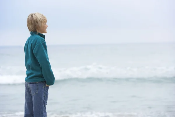 Giovane ragazzo in vacanza in piedi sulla spiaggia invernale guardando verso il mare — Foto Stock