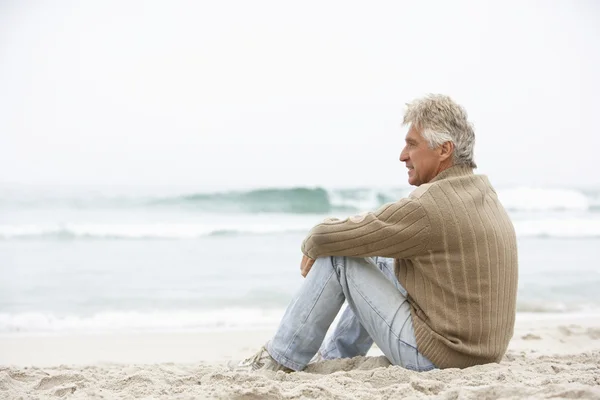 Starszy mężczyzna siedzi na plaży zimowych wakacji — Zdjęcie stockowe
