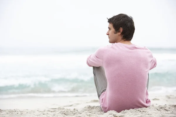 Młody człowiek siedzi na plaży zimowych wakacji — Zdjęcie stockowe