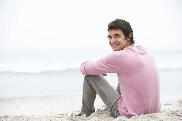 Young Man On Holiday Sitting On Winter Beach — Stock Photo, Image